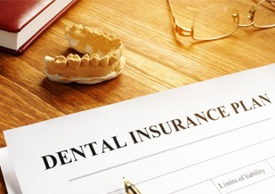 Dental insurance form on a desk with glasses and model of teeth