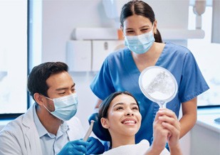 Patient smiling at reflection next to dentist and dental assistant