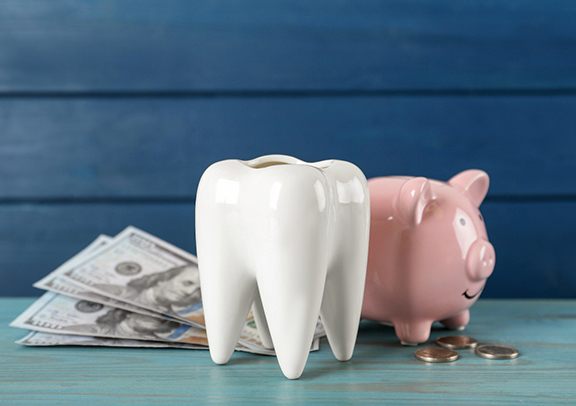 A ceramic tooth model, piggy bank and money on a light blue wooden table