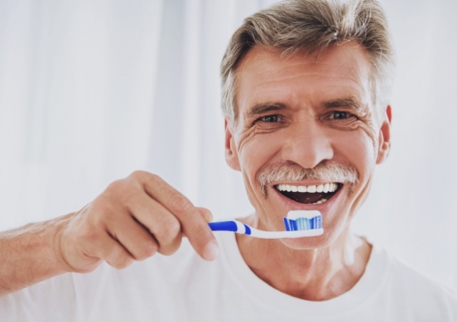 Man brushing teeth to maintain dentures