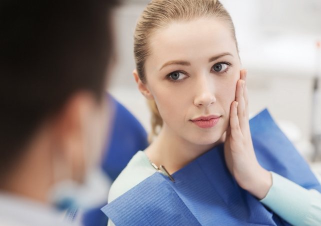 Woman in need of emergency dentistry holding cheek in pain