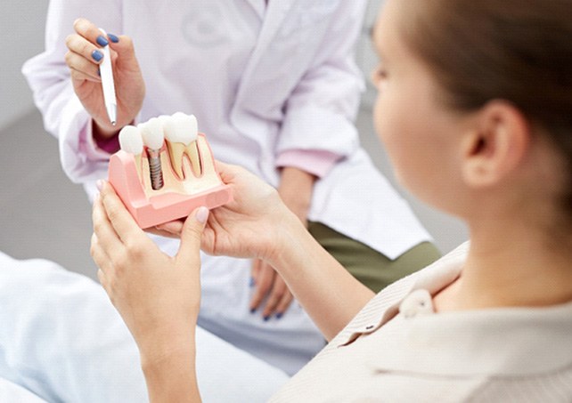 A dentist showing a dental implant model to a patient