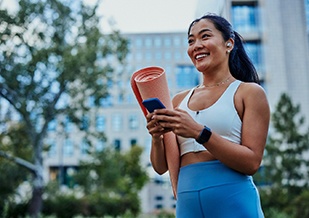 Smiling woman with yoga mat walking in park