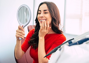 Woman in red shirt smiling at reflection in handheld mirror