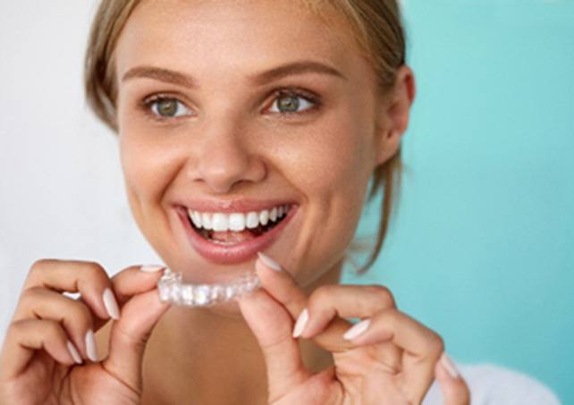 Woman smiling while holding at-home teeth whitening tray