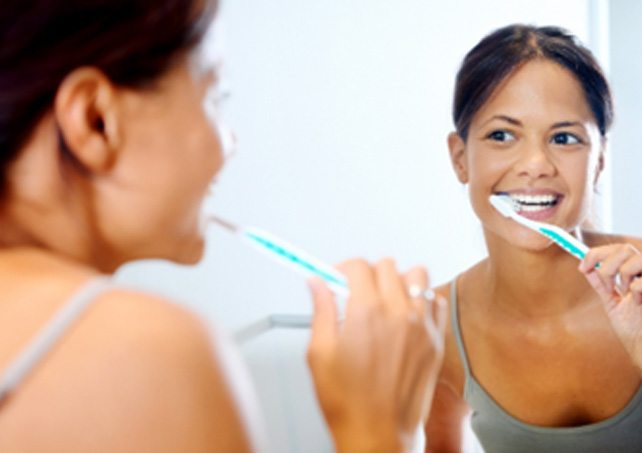 Woman smiling while brushing her teeth in mirror