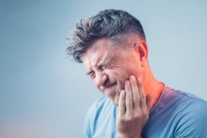 man holding mouth in pain who needs emergency dentist 