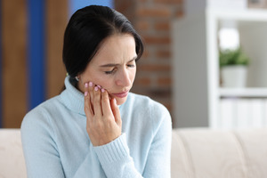 Woman in light blue sweater sitting on a couch with jaw pain
