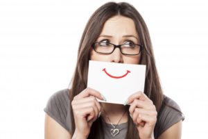 a woman hiding her smile behind a white card with a red smile drawn on it